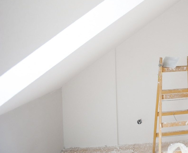 Sloped attic ceiling in white with daylight across it and a timber step ladder against the wall