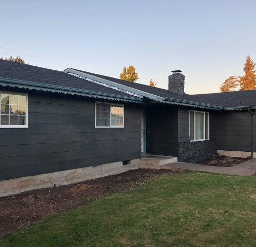 Single story house finished in a dark charcoal with white window trim
