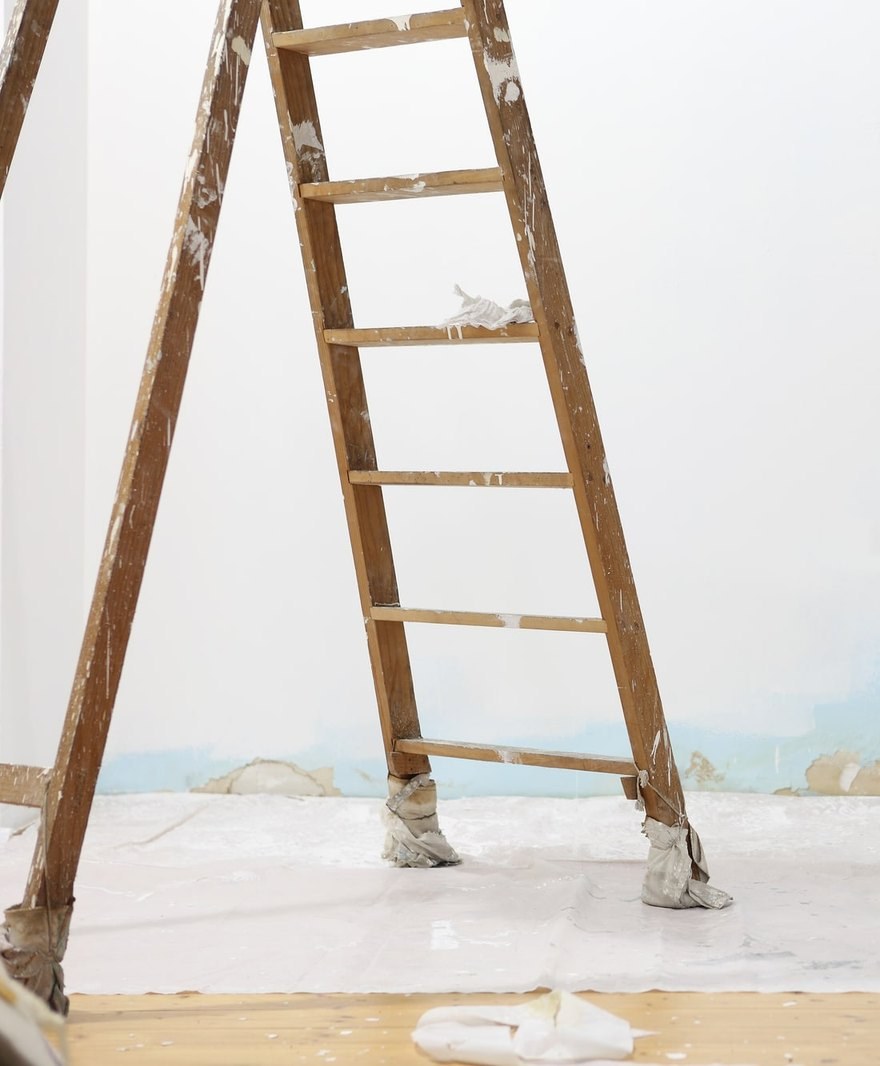 Timber step ladder on dust sheets against a white wall with blue showing at the skirting