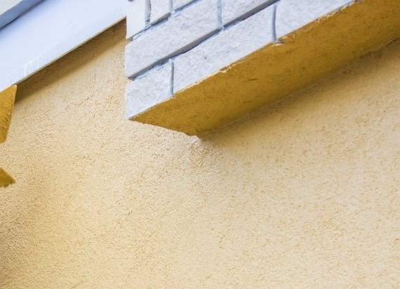 Yellow rendered wall meeting a gray brick sill and a molded band under the eaves