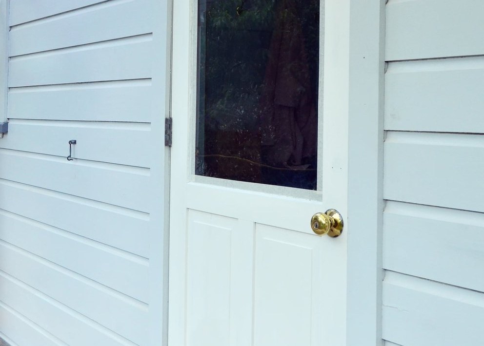 Pale blue lap siding beside a glazed paneled door with a brass knob and a cast iron hook