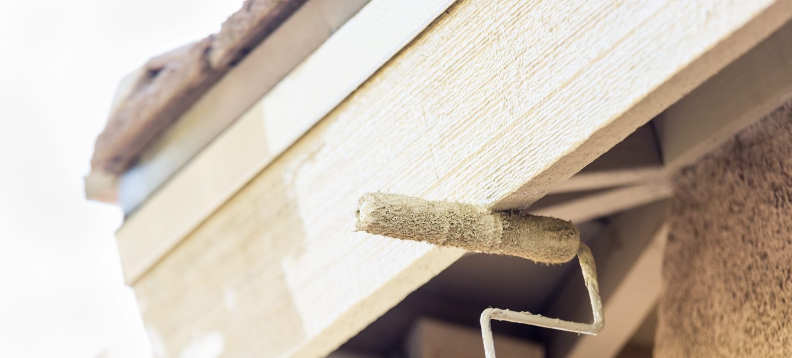 Roller loaded with cream paint resting against timber lap siding