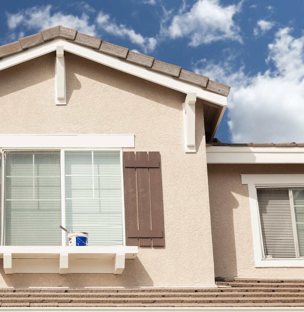Stucco gable with white trim and a brown board shutter, a paint can resting on the window sill