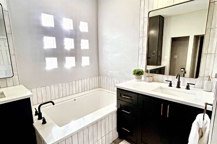 Pale gray walls over a tiled tub with a glass block window and a black shaker vanity