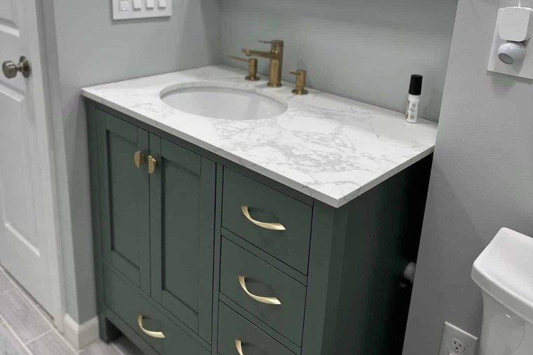Green vanity with brass pulls and a marble look top against pale sage walls