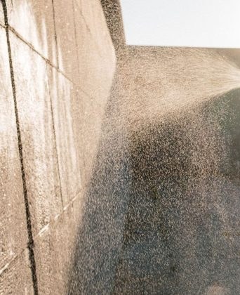 Pressure washer spray fanning across a rendered exterior wall