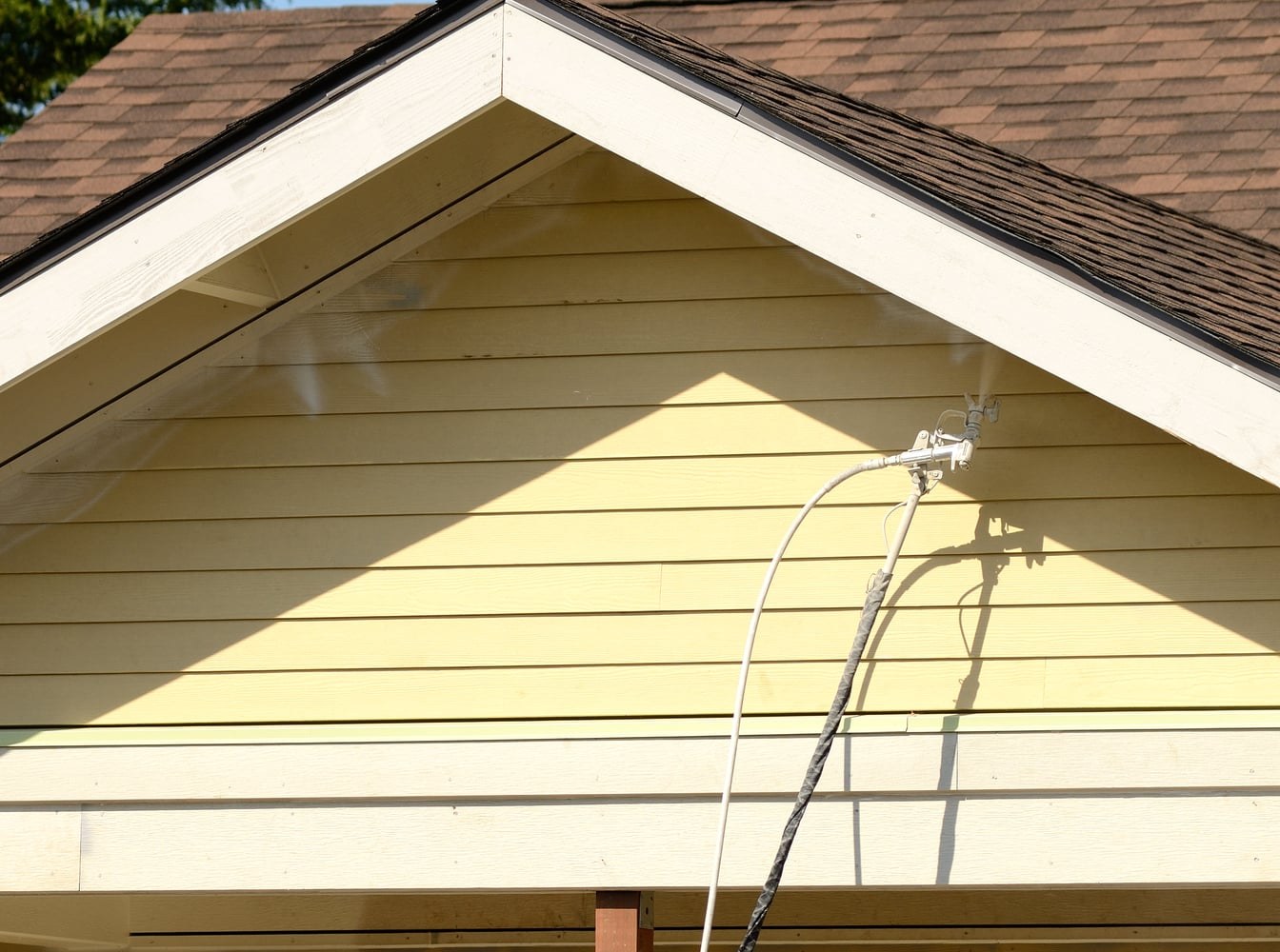Yellow gable end and lap siding under a spray gun working up toward the roofline