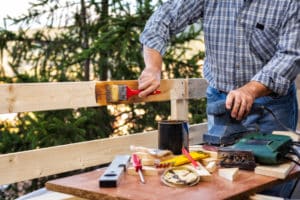 Adult craftsman carpenter with the brush painting the boards of a wooden fence. Housework do it yourself. Stock Photography.