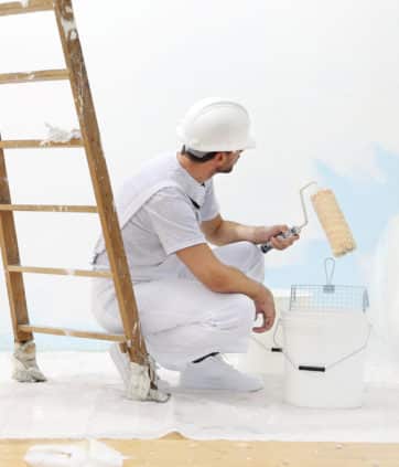 A man at work takes the color with a paint roller from the bucket - Big Easy Paintings